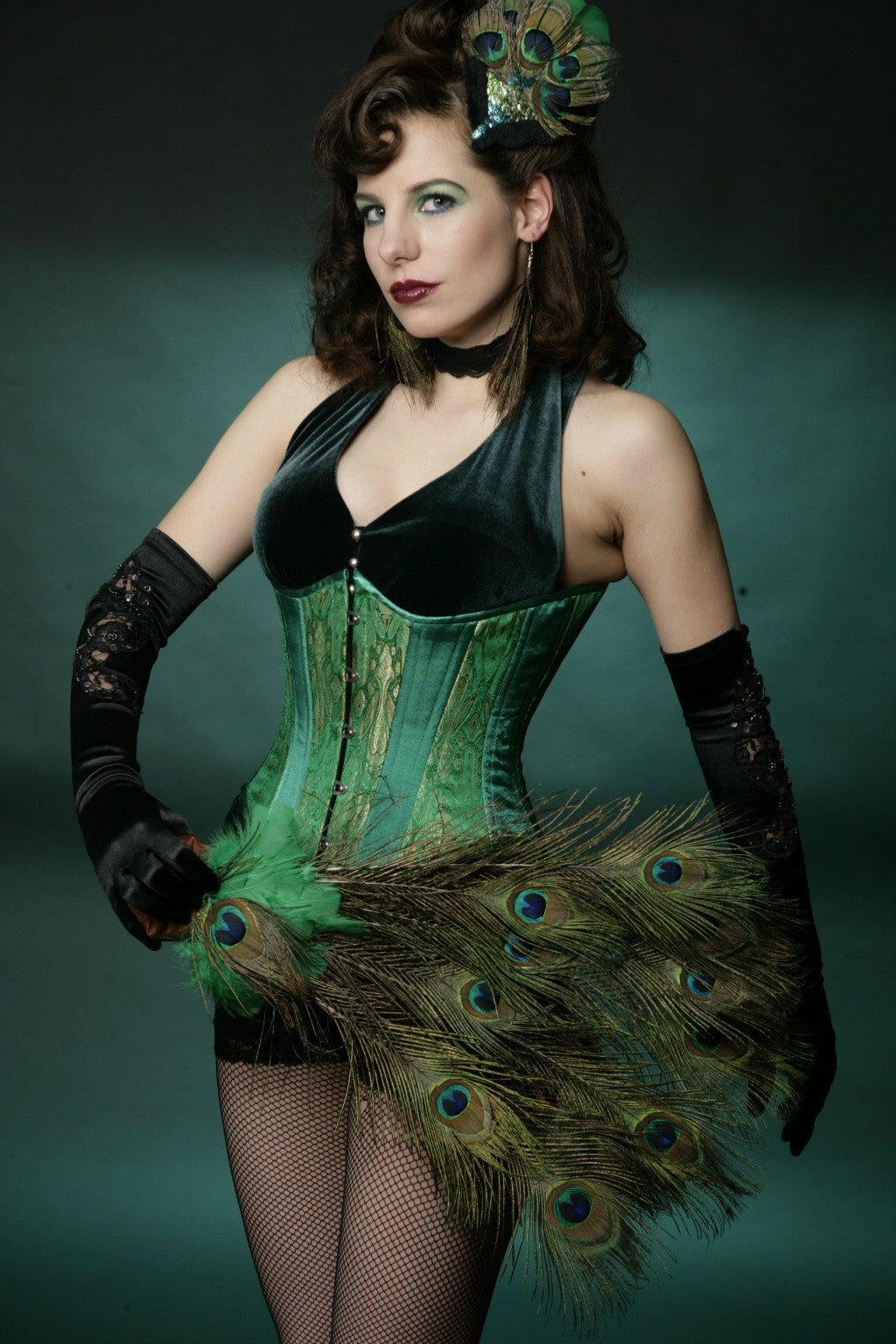 Emerald and gold brocade corset, slim silhouette, regular underbust length, on model with green velvet suit and peacock feathers