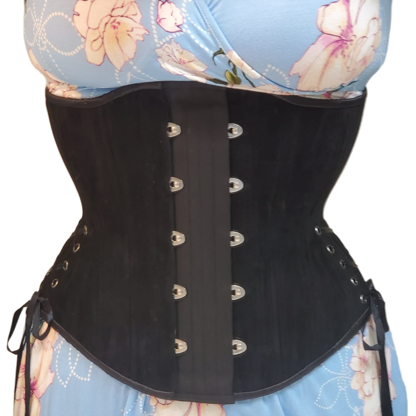 Person wearing a black waist training corset with a 2-inch wide expander panel, over a floral top on a white background
